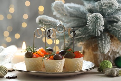 Photo of Tasty canapes and festive decor on white table against blurred lights, closeup. Bokeh effect