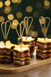 Photo of Tasty canapes with cheese on wooden table against blurred lights, closeup. Bokeh effect