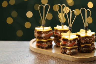Photo of Tasty canapes with cheese on wooden table against blurred lights, closeup. Space for text