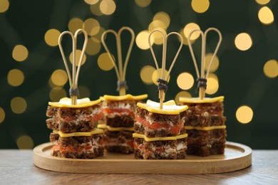 Photo of Tasty canapes with cheese on wooden table against blurred lights, closeup. Bokeh effect