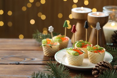 Photo of Tasty canapes and festive decor on wooden table against blurred lights, closeup. Space for text