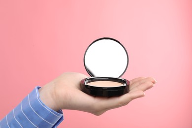 Photo of Woman holding open face powder with mirror on pink background, closeup