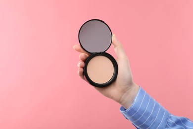 Photo of Woman holding open face powder with mirror on pink background, closeup. Space for text