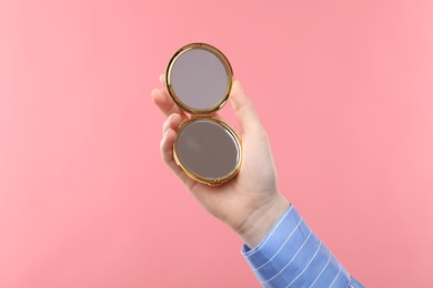 Photo of Woman holding open pocket mirror on pink background, closeup