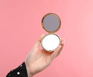 Photo of Woman holding open pocket mirror on pink background, closeup