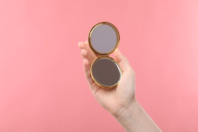 Photo of Woman holding open pocket mirror on pink background, closeup. Space for text