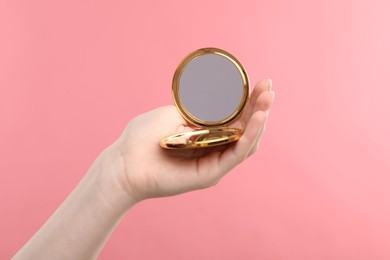 Photo of Woman holding open pocket mirror on pink background, closeup
