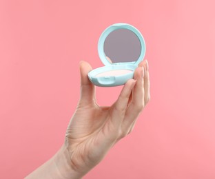 Photo of Woman holding open face powder with mirror on pink background, closeup
