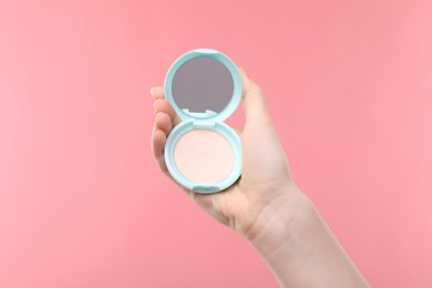 Photo of Woman holding open face powder with mirror on pink background, closeup