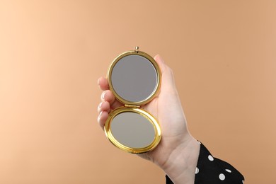 Photo of Woman holding open pocket mirror on beige background, closeup