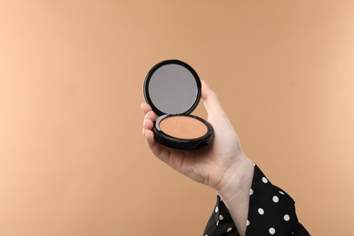 Photo of Woman holding open face powder with mirror on beige background, closeup
