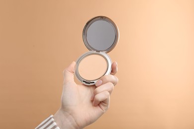 Photo of Woman holding open face powder with mirror on beige background, closeup