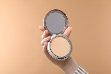 Photo of Woman holding open face powder with mirror on beige background, closeup