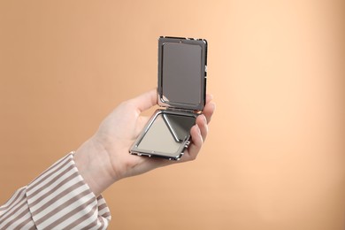 Photo of Woman holding open pocket mirror on beige background, closeup