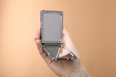 Photo of Woman holding open pocket mirror on beige background, closeup