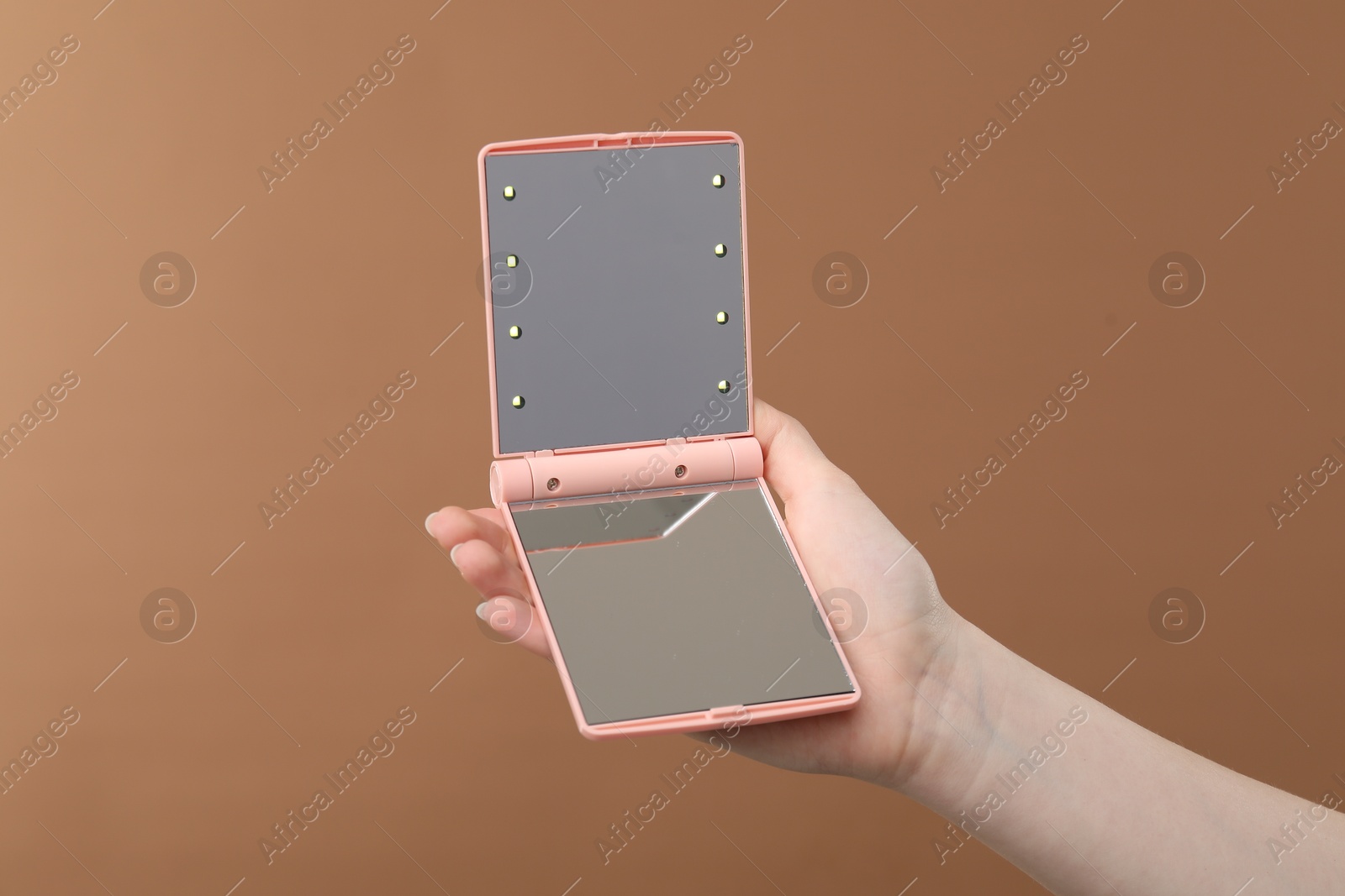 Woman holding open pocket mirror on brown background, closeup Photo of Woman holding open pocket mirror on brown background, closeup