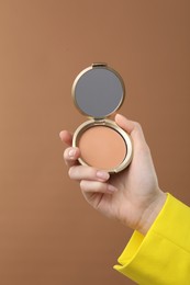 Photo of Woman holding open face powder with mirror on brown background, closeup
