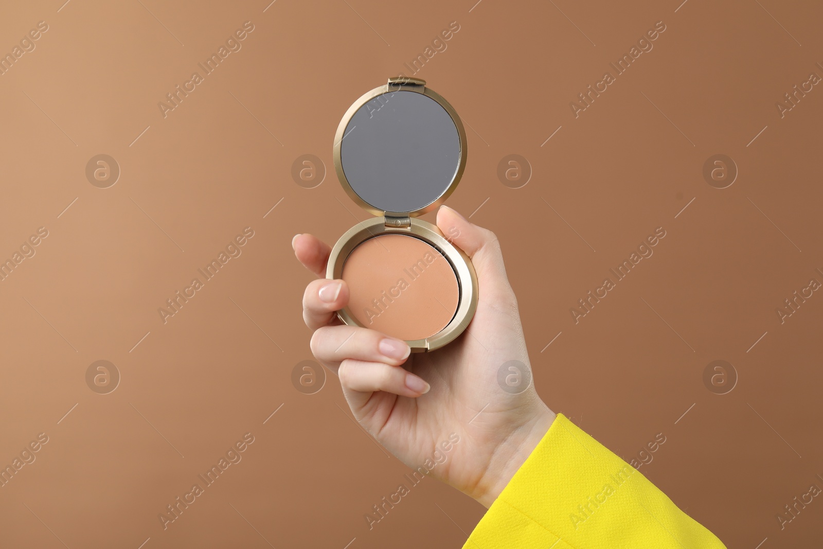 Woman holding open face powder with mirror on brown background, closeup Photo of Woman holding open face powder with mirror on brown background, closeup