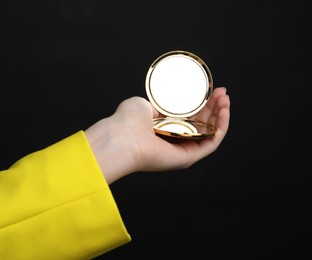 Photo of Woman holding open pocket mirror on black background, closeup
