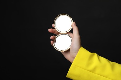 Photo of Woman holding open pocket mirror on black background, closeup