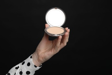 Photo of Woman holding open face powder with mirror on black background, closeup