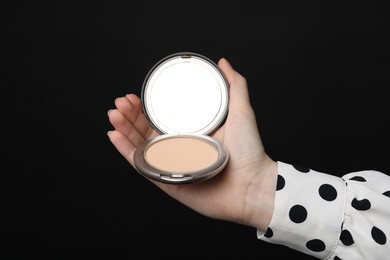 Photo of Woman holding open face powder with mirror on black background, closeup