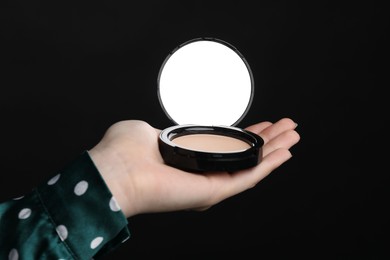 Photo of Woman holding open face powder with mirror on black background, closeup