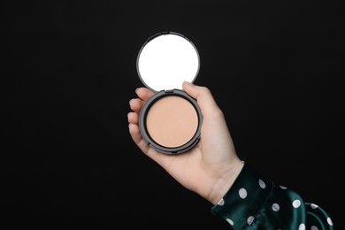 Photo of Woman holding open face powder with mirror on black background, closeup