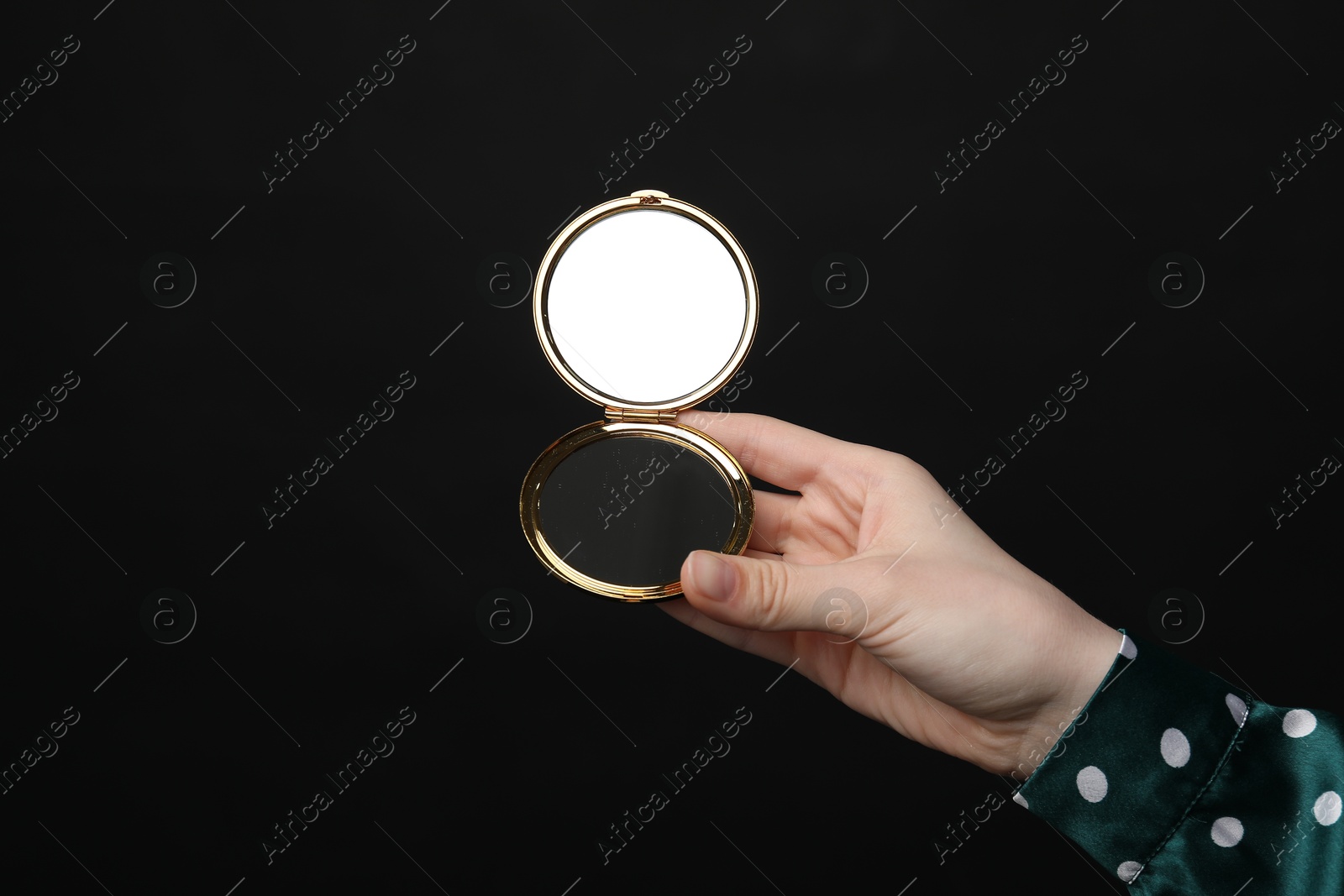 Photo of Woman holding open pocket mirror on black background, closeup
