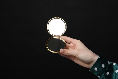 Photo of Woman holding open pocket mirror on black background, closeup