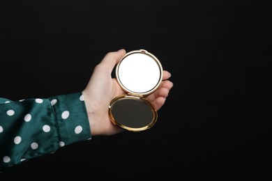 Photo of Woman holding open pocket mirror on black background, closeup