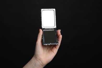 Photo of Woman holding open pocket mirror on black background, closeup