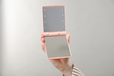 Photo of Woman holding open pocket mirror on grey background, closeup