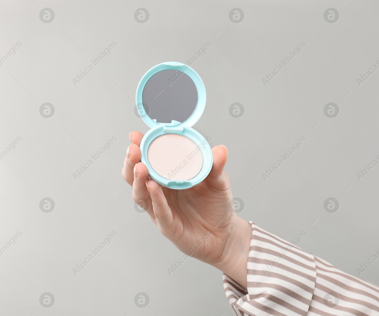 Woman holding open face powder with mirror on grey background, closeup Photo of Woman holding open face powder with mirror on grey background, closeup