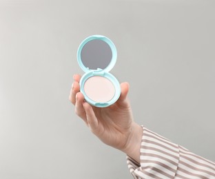 Photo of Woman holding open face powder with mirror on grey background, closeup