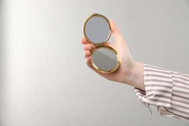 Photo of Woman holding open pocket mirror on grey background, closeup. Space for text