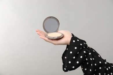 Photo of Woman holding open face powder with mirror on grey background, closeup. Space for text