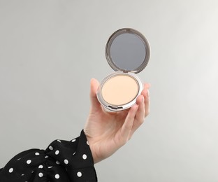Photo of Woman holding open face powder with mirror on grey background, closeup