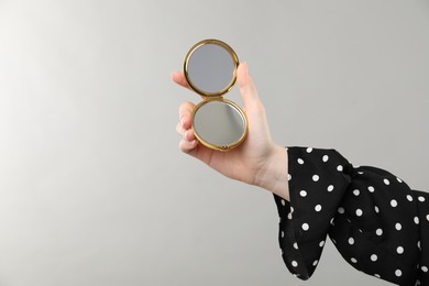 Photo of Woman holding open pocket mirror on grey background, closeup. Space for text