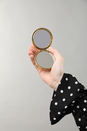 Photo of Woman holding open pocket mirror on grey background, closeup