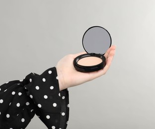 Photo of Woman holding open face powder with mirror on grey background, closeup