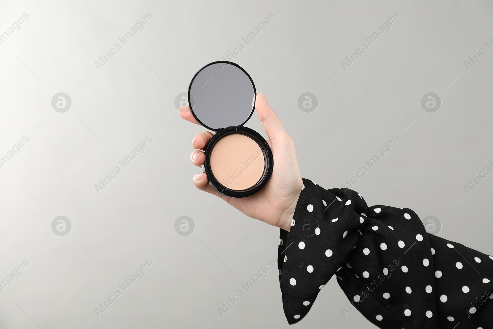 Woman holding open face powder with mirror on grey background, closeup. Space for text Photo of Woman holding open face powder with mirror on grey background, closeup. Space for text