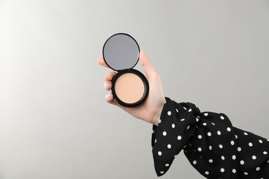 Photo of Woman holding open face powder with mirror on grey background, closeup. Space for text