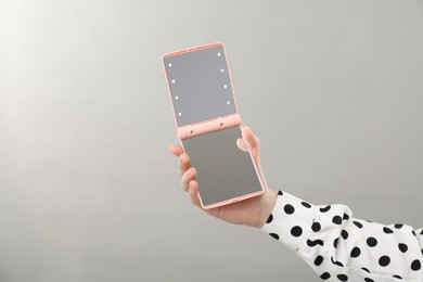 Photo of Woman holding open pocket mirror on grey background, closeup. Space for text