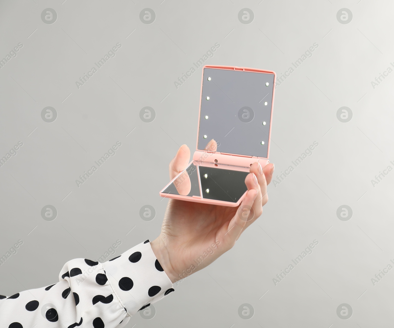 Photo of Woman holding open pocket mirror on grey background, closeup