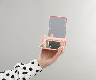 Photo of Woman holding open pocket mirror on grey background, closeup