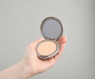 Photo of Woman holding open face powder with mirror on grey background, closeup