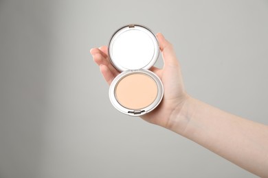 Photo of Woman holding open face powder with mirror on grey background, closeup. Space for text
