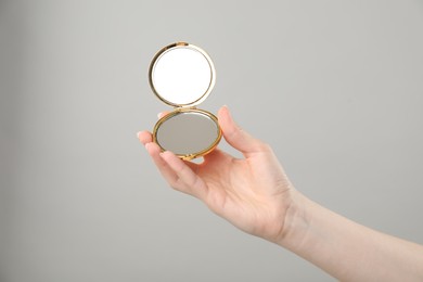 Photo of Woman holding open pocket mirror on grey background, closeup