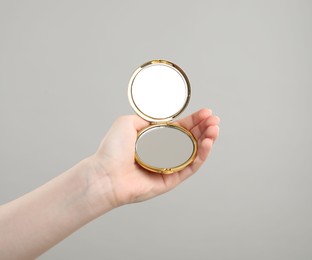 Photo of Woman holding open pocket mirror on grey background, closeup